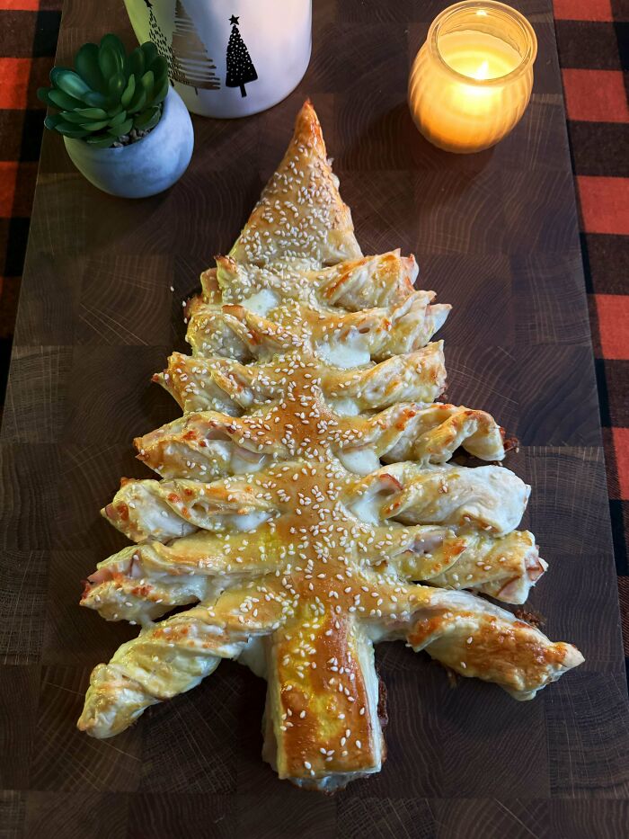 Christmas snack shaped like a tree, made from pastry and sprinkled with sesame seeds, on a wooden board with candle.