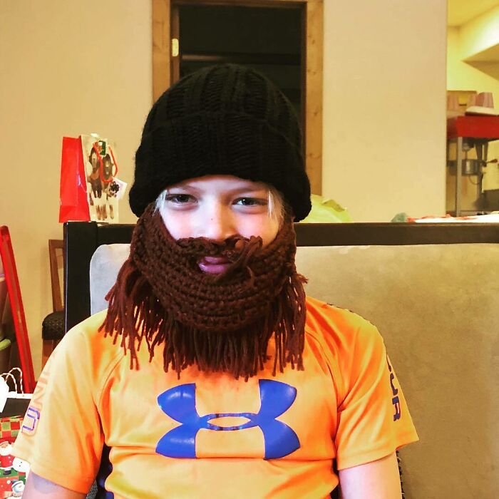 Child wearing a knitted beard and hat, showcasing a funny trolling Christmas gift.