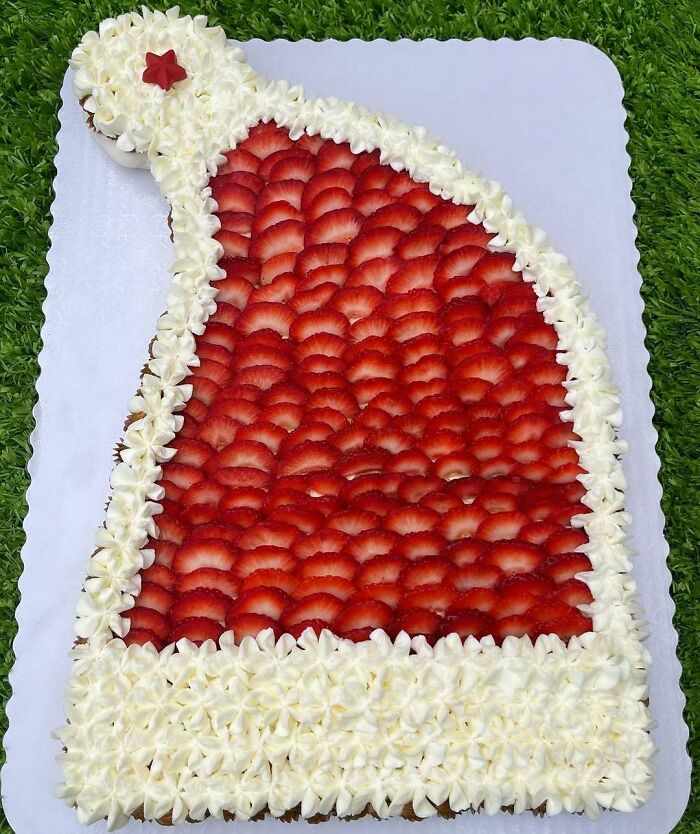 Decorative Christmas snack shaped like a Santa hat with strawberries and cream on grass background.