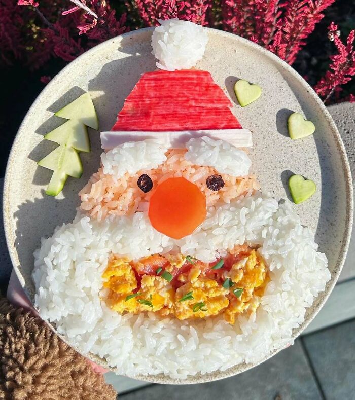 Festive Christmas snack food shaped like Santa using rice, egg, and vegetables on a plate with heart and tree decorations.