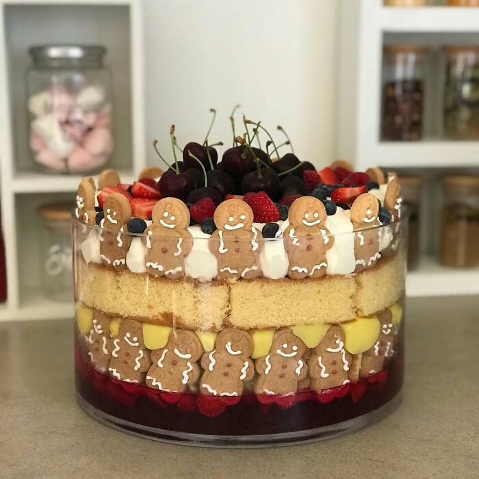 Layered Christmas snack with sponge cake, gingerbread cookies, cream, and assorted berries in a glass bowl.