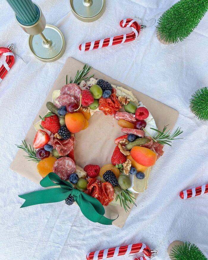 Festive Christmas snack wreath with fruits, meats, and cheese on a white tablecloth, surrounded by candy canes.