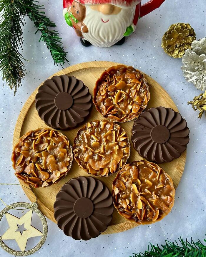 Christmas snack food ideas with chocolate and nut tarts on a wooden plate, surrounded by festive decor.