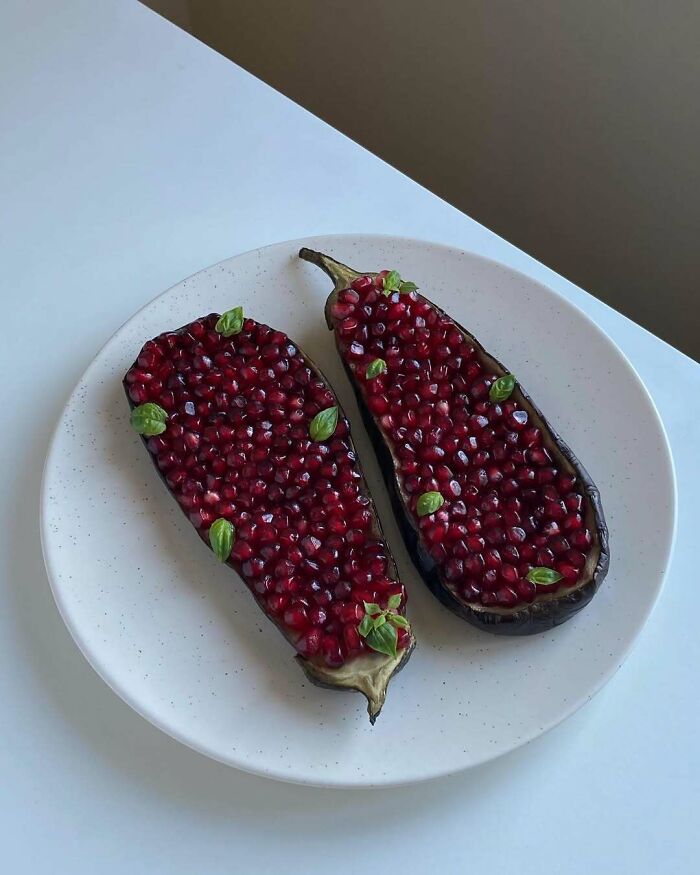 Christmas snack food idea with pomegranate seeds and basil leaves on a sliced eggplant, arranged on a white plate.