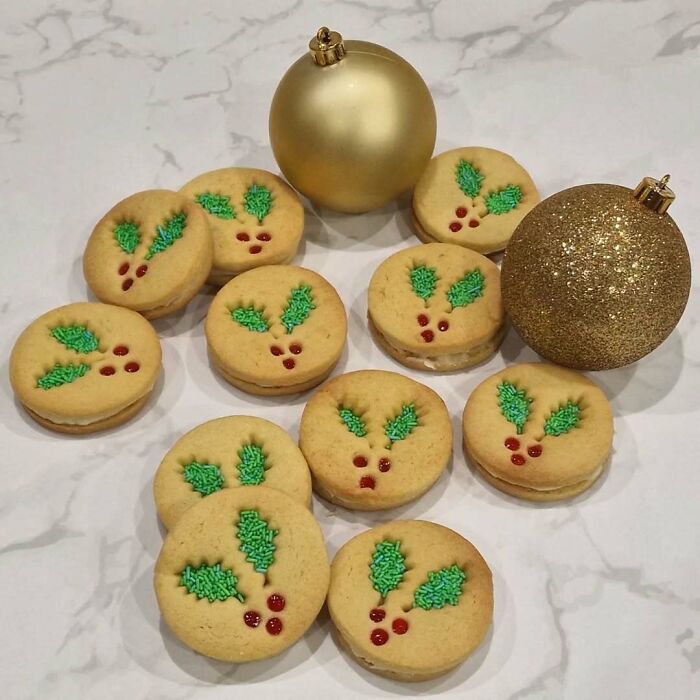 Christmas snack food with holly-decorated cookies and gold ornaments on a marble surface.