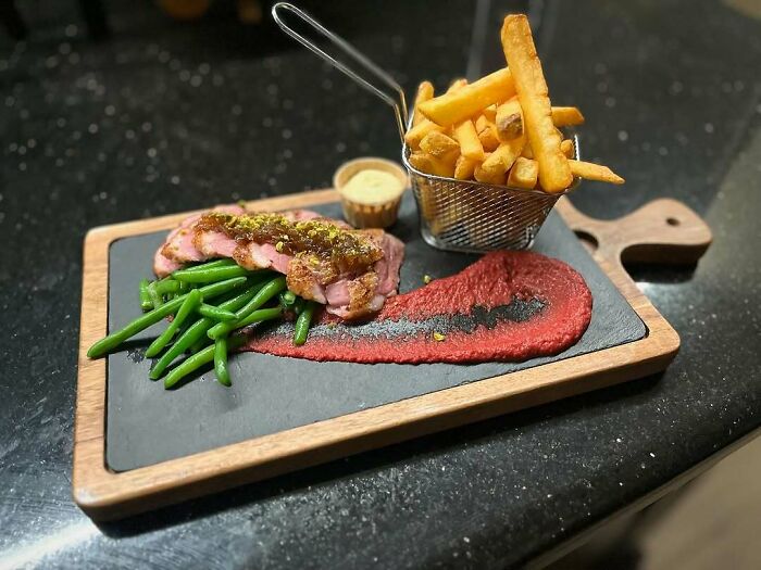 Gourmet Christmas snack with steak, green beans, beet puree, and fries on a wooden platter.