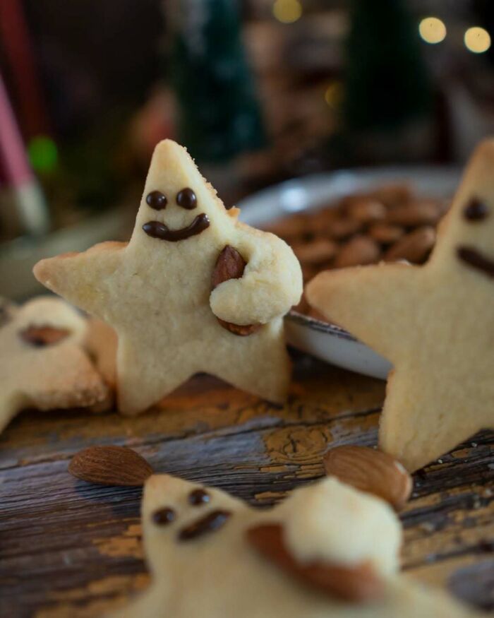 Star-shaped Christmas snack cookies with chocolate faces and almonds as decoration on a festive table.