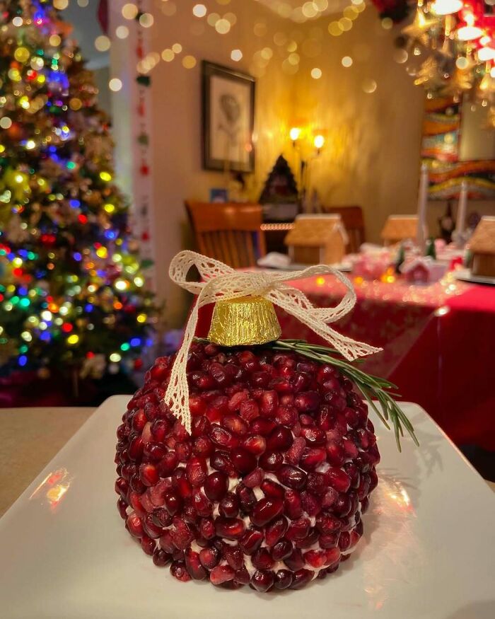 Festive Christmas snack resembling an ornament made of pomegranate seeds with a holiday dinner setup in the background.