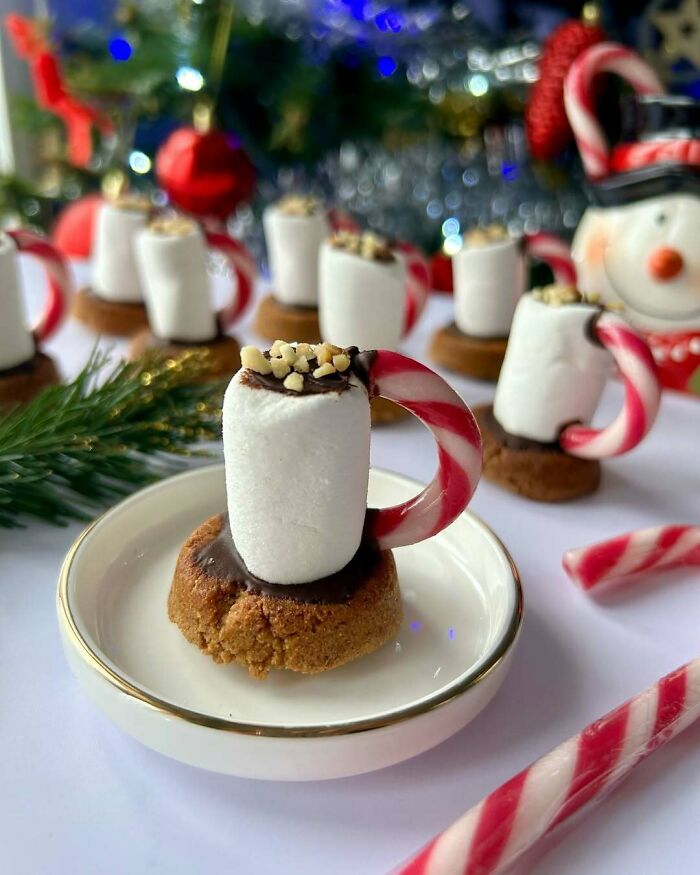 Mini marshmallow mugs with candy cane handles on cookies, festive Christmas snack food ideas.