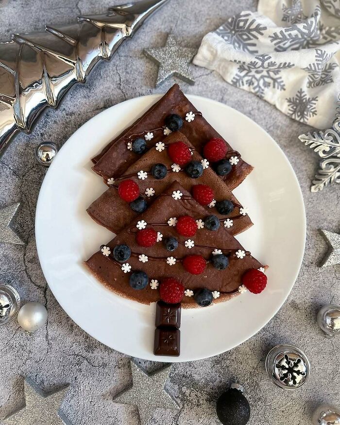 Christmas snack with crepes arranged as a tree, garnished with berries and chocolate, on a festive plate.