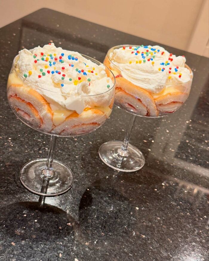 Festive Christmas snack with whipped cream and sprinkles in glass cups on a dark countertop.