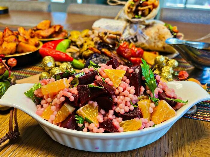 Christmas snack food ideas with colorful salad in a white dish, surrounded by various festive treats on a wooden table.