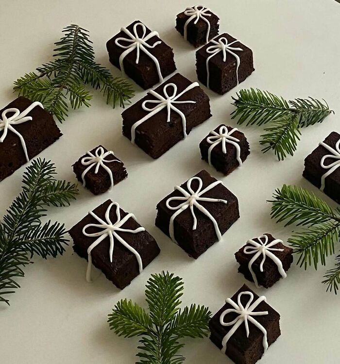 Chocolate snacks decorated as gift boxes with white icing and surrounded by evergreen sprigs, perfect for Christmas snack ideas.