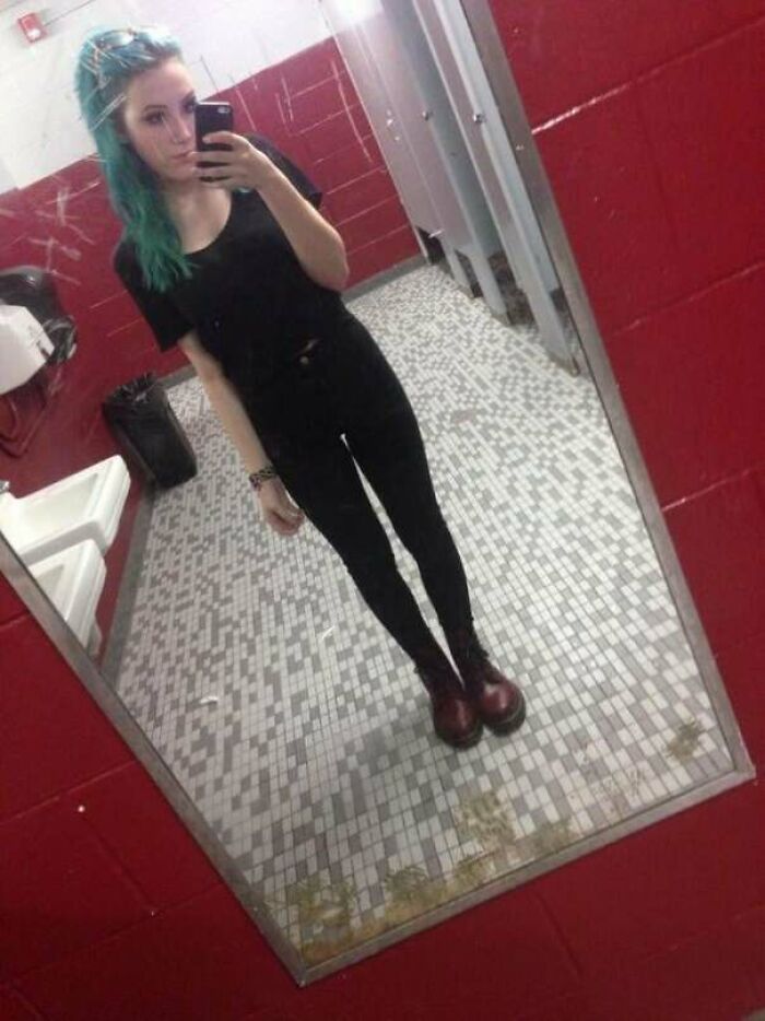 Person taking a mirror selfie in a bathroom with green hair and black outfit, fitting the theme of blunder years photos.