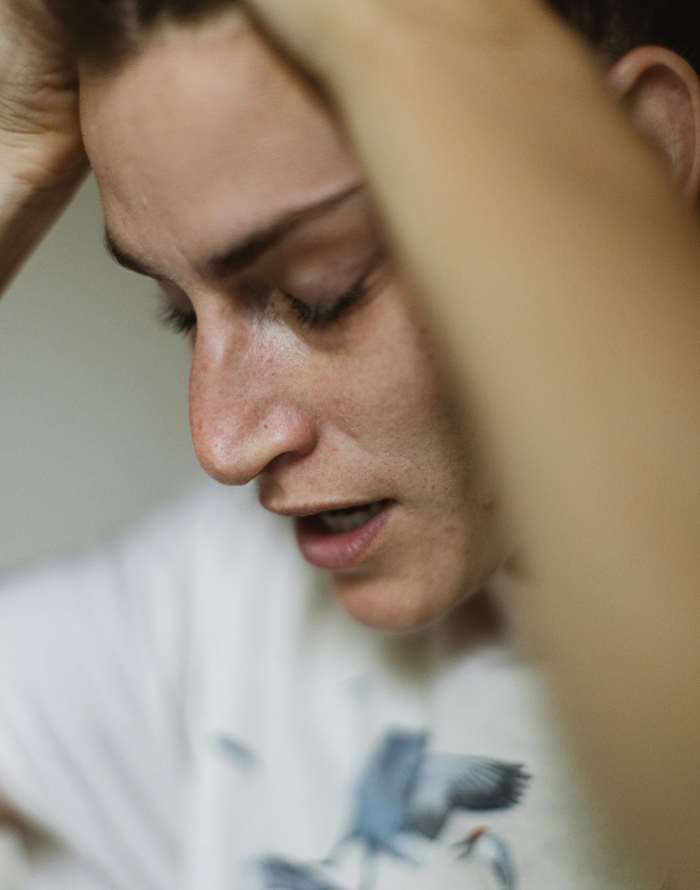 A stressed mother holds her head, defending her daughter amid family conflict over her baby's care.