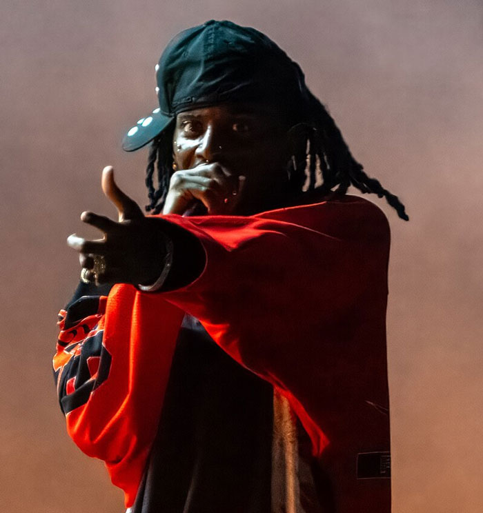 A singer in a red jacket and cap performing with a microphone passionately on stage.