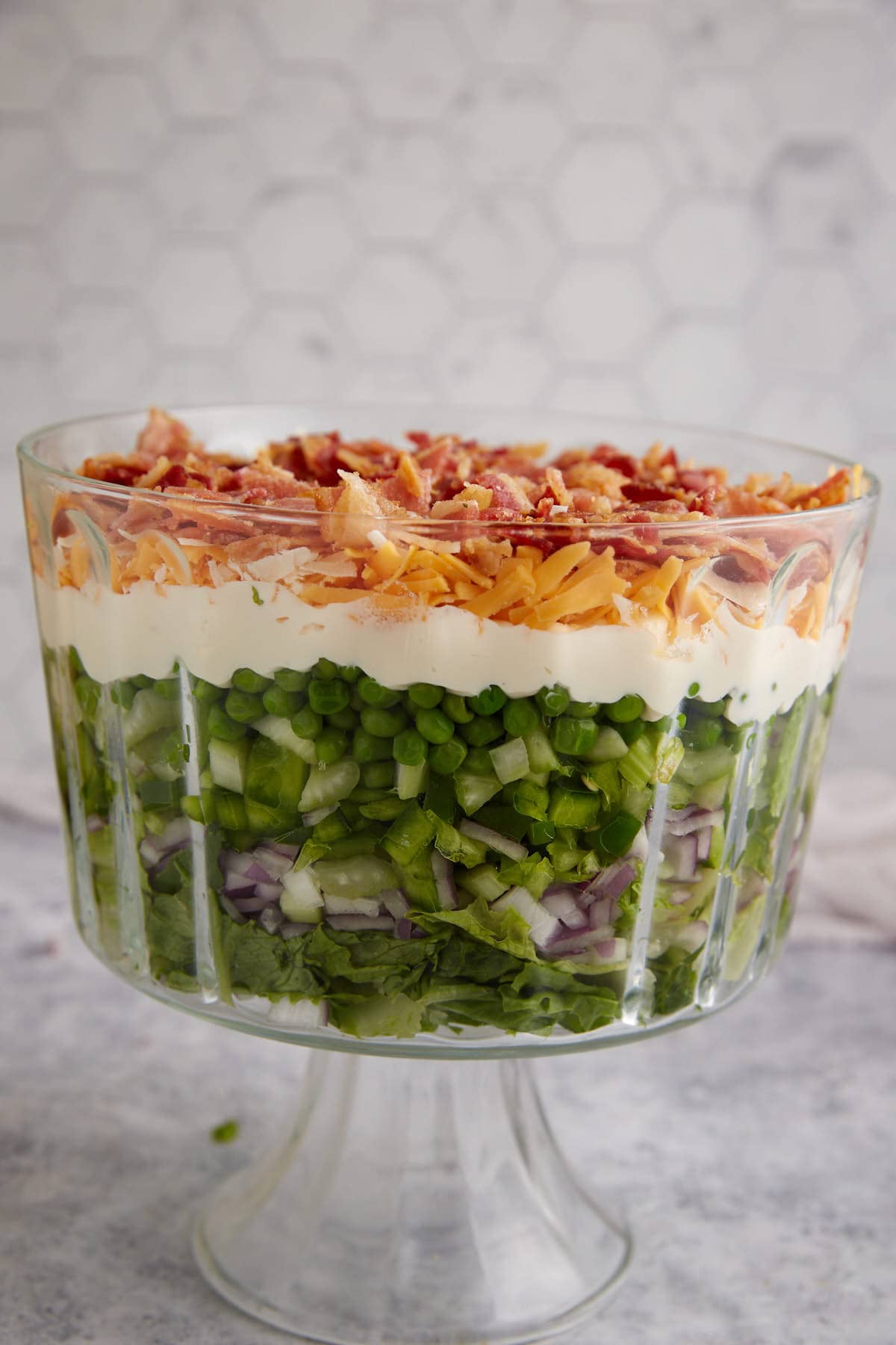 An assembled 7 layer salad in a trifle bowl.