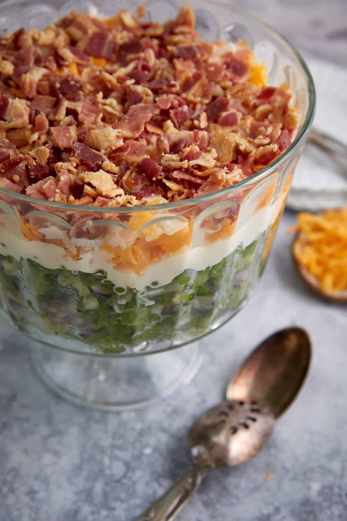 A bowl of 7 layer salad next to a serving spoon.