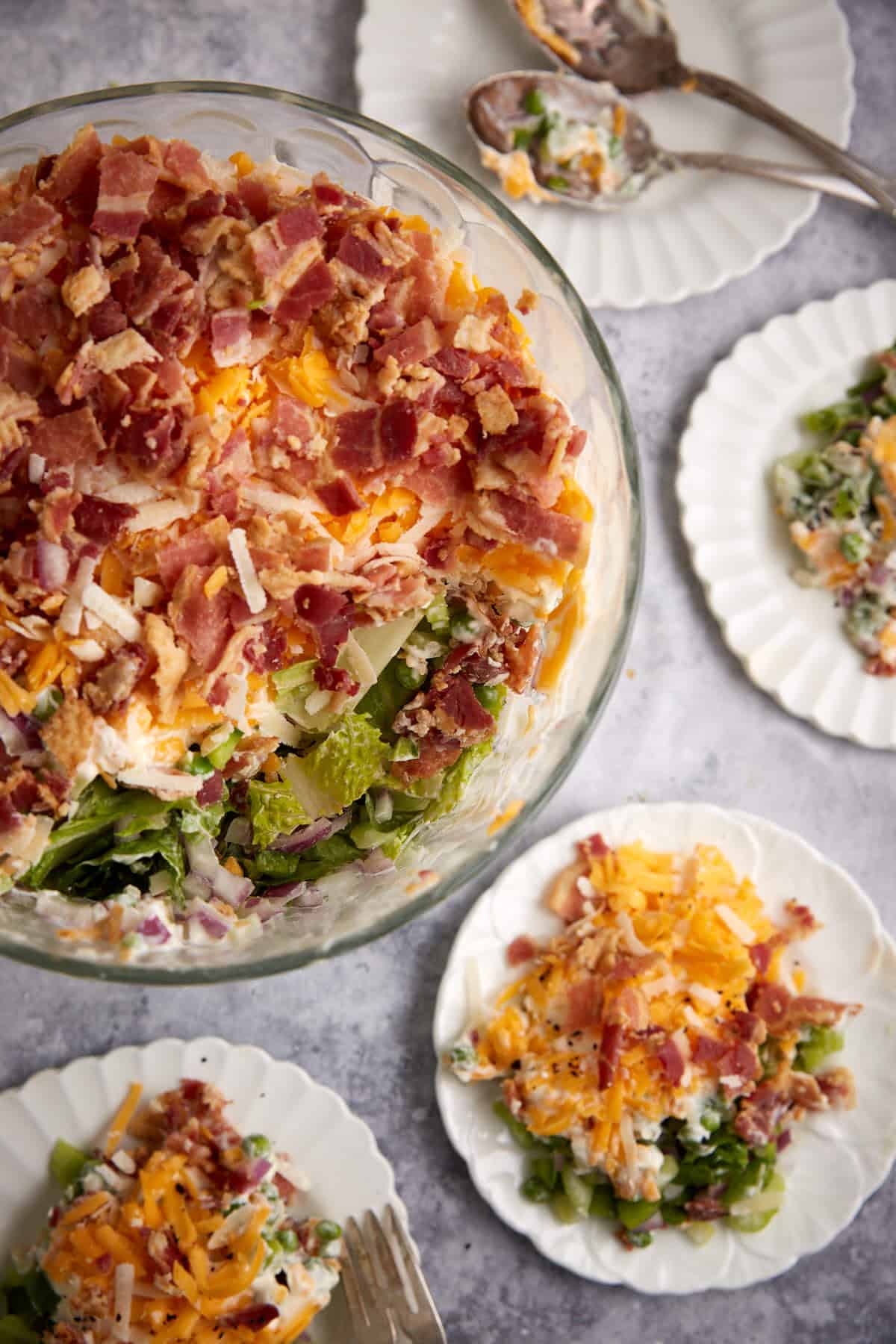 A bowl of seven layer salad next to individual servings.