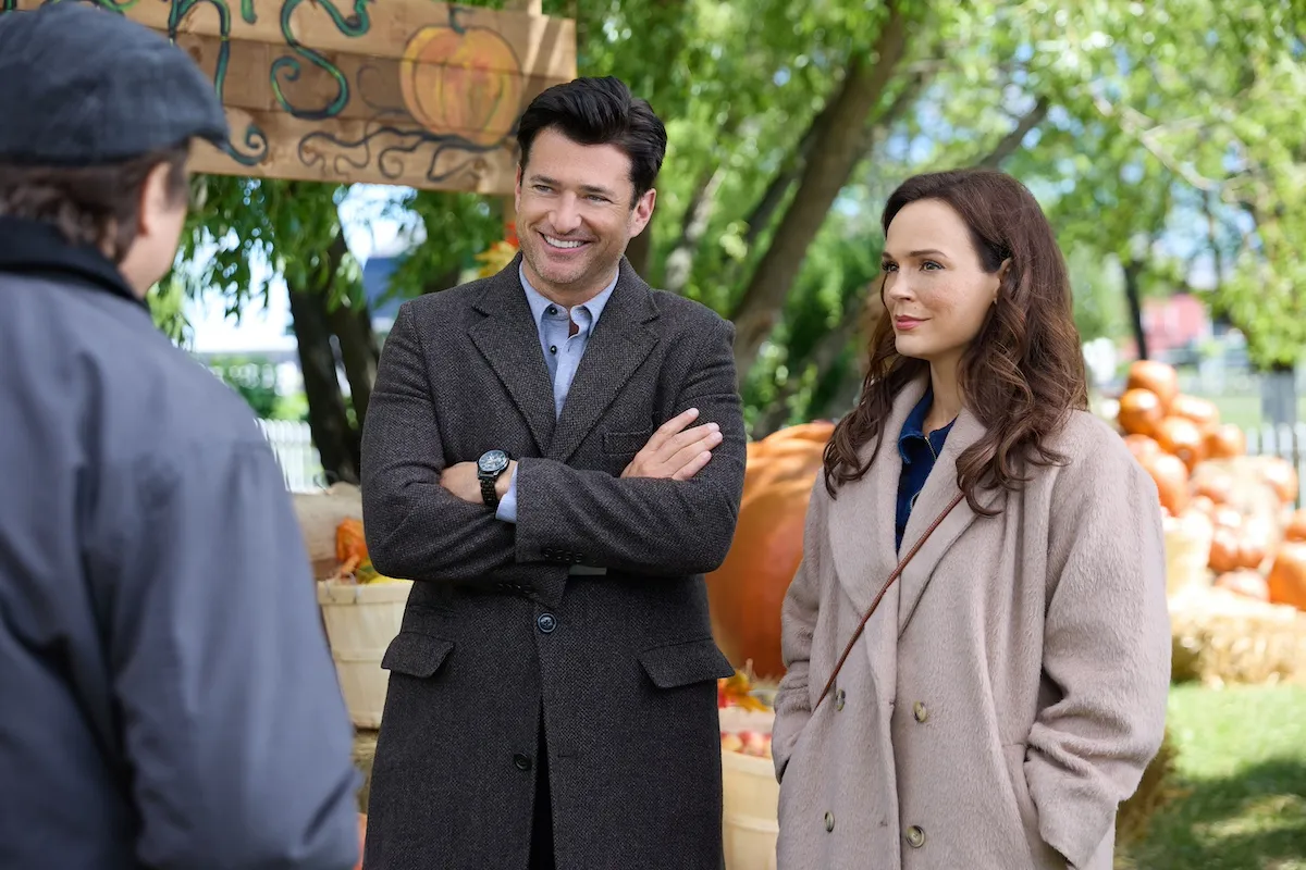 Man and woman standing in front of a display of pumpkins in the Hallmark movie 'Autumn at Apple Hill'