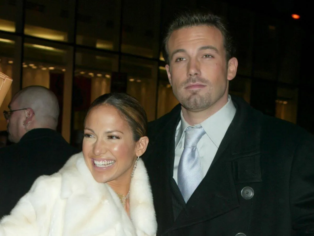 Jennifer Lopez wears a white fur coat and stands with Ben Affleck, who wears a suit.