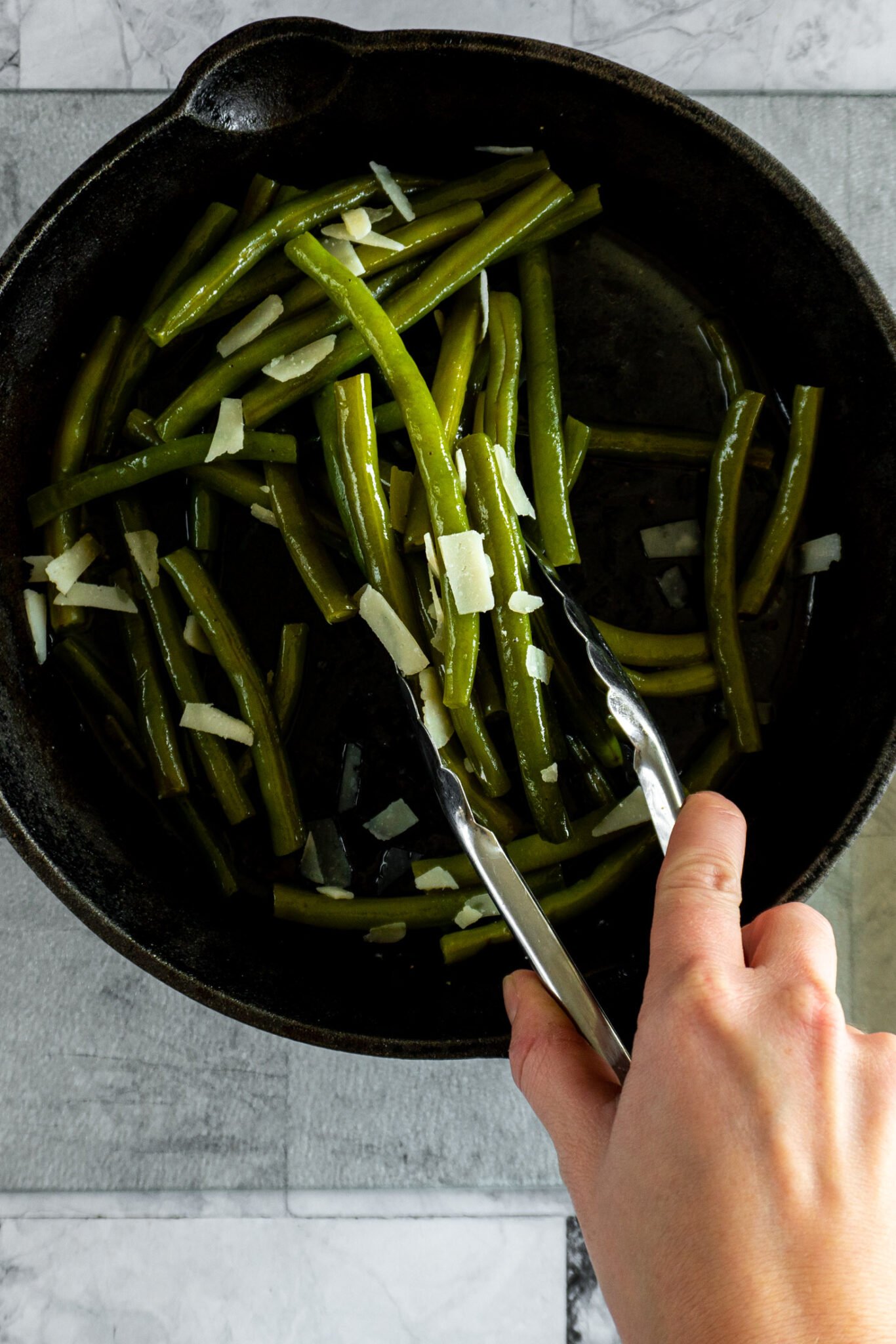 xPicking up the green beans with tongs to move to serving tray.