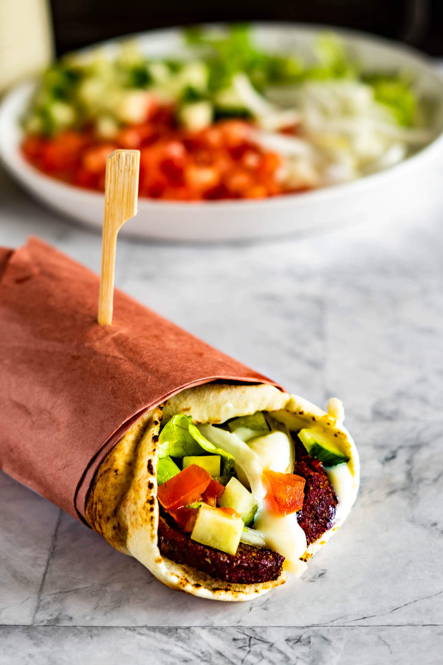 A wrapped donair in front of a plate of chopped veggies.