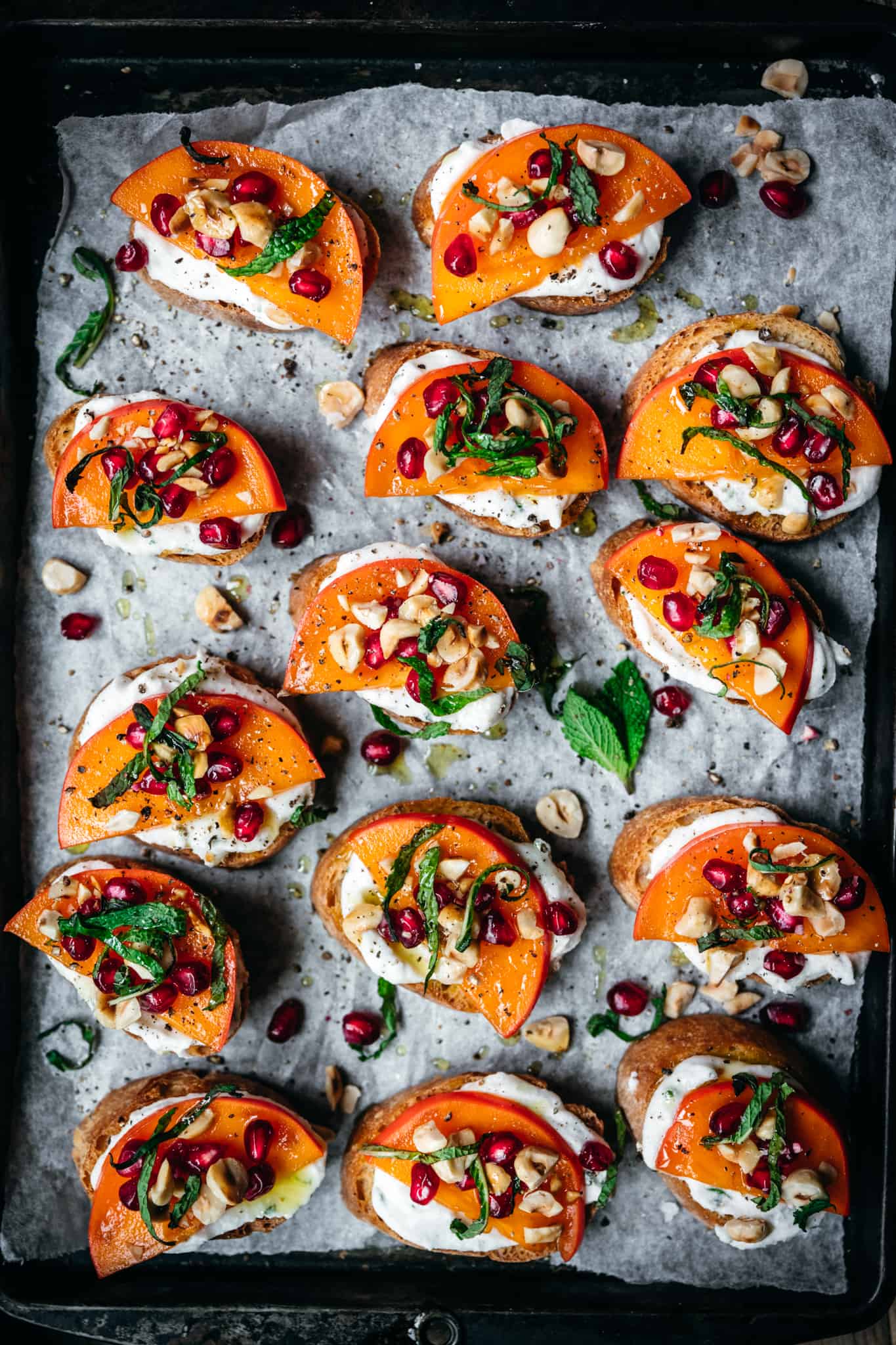 overhead of vegan crostini with persimmon and pomegranate on a baking sheet