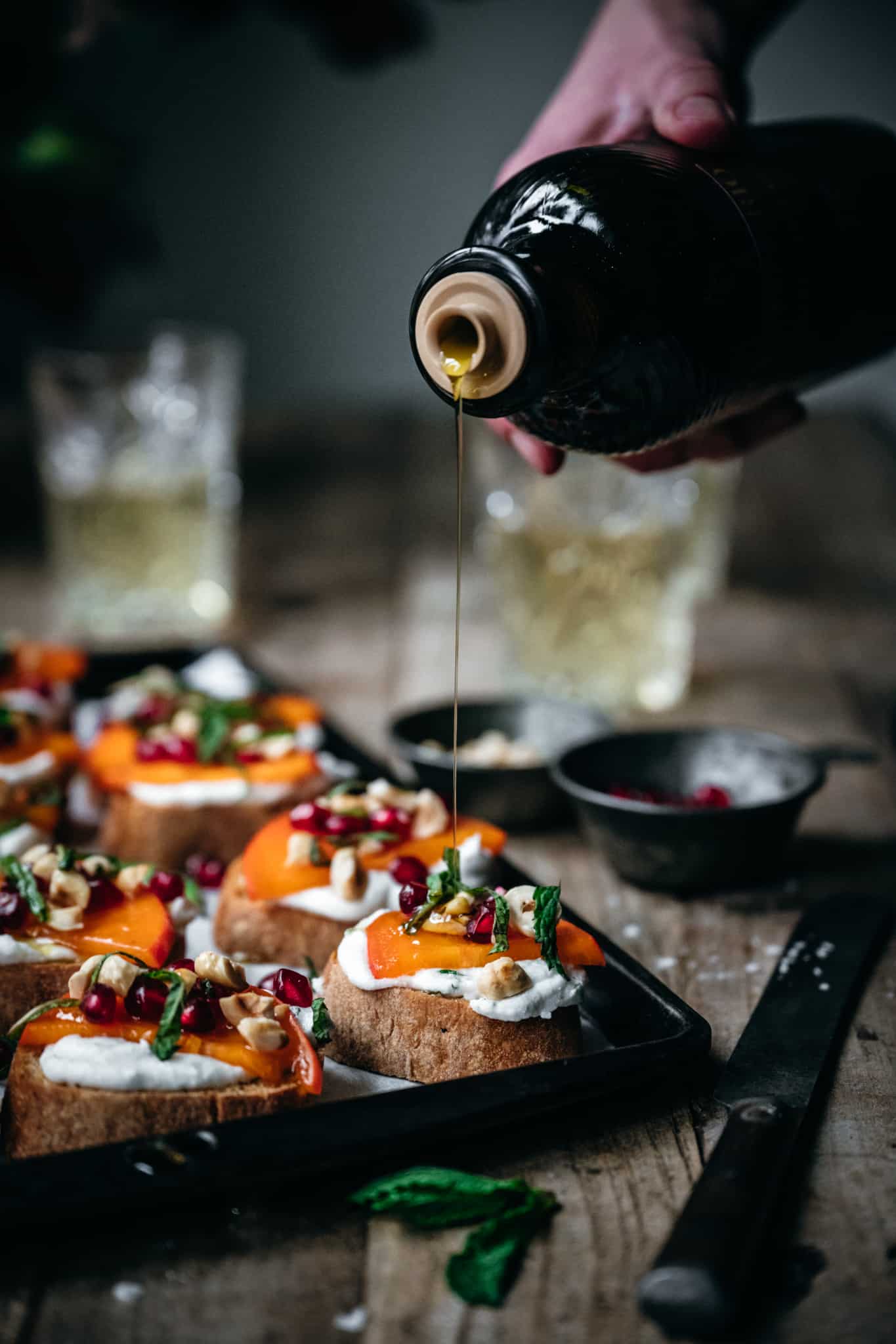 side view of a person drizzling the vegan crostini appetizers with olive oil