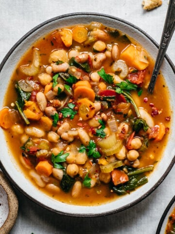 close up overhead view of vegan bean soup in a bowl on white linen surface.