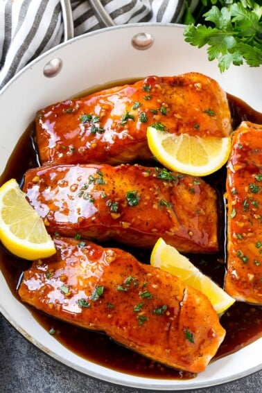 A pan of honey garlic salmon topped with a savory sauce and garnished with parsley and lemon.