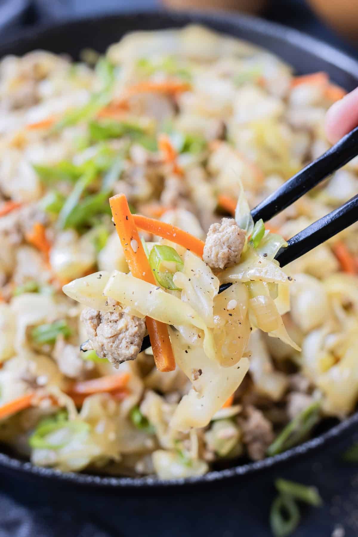 Chopsticks are used to dig into a serving of egg roll in a bowl.