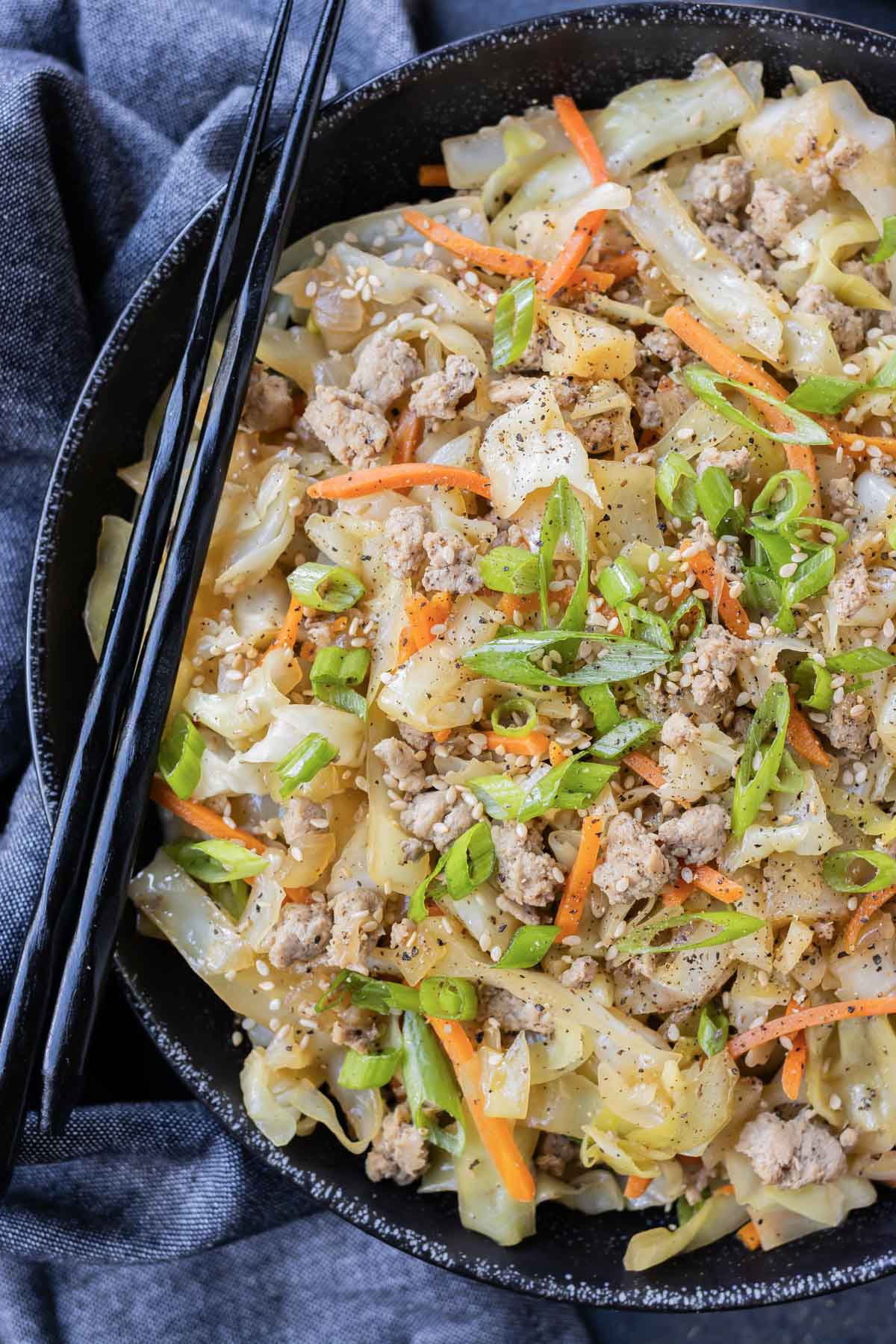 A low-carb egg roll bowl is in a black bowl with green onions.