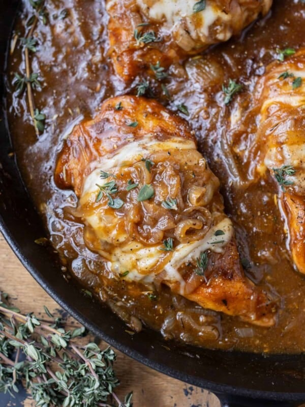 French onion chicken in a cast iron skillet with caramelized onions, gruyere cheese, and fresh thyme on top.