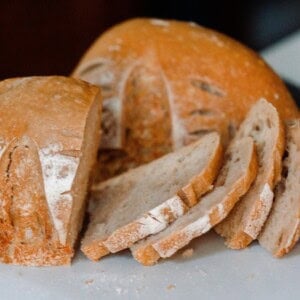 A sourdough boule cut into two halves with one cut into slices on white countertop with knife in background