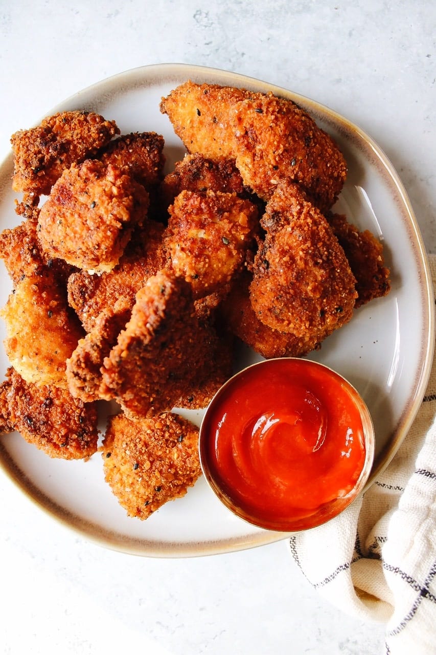 Homemade chicken nuggets on a white plate with ketchup