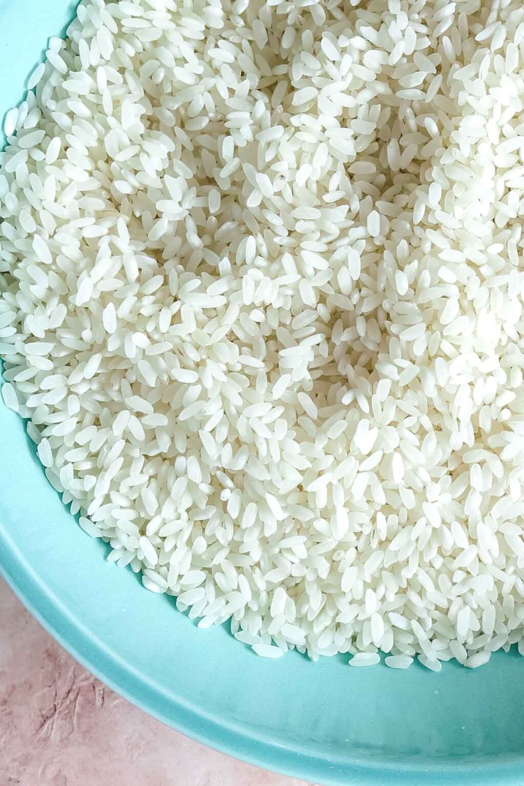 uncooked medium grain rice in a teal bowl
