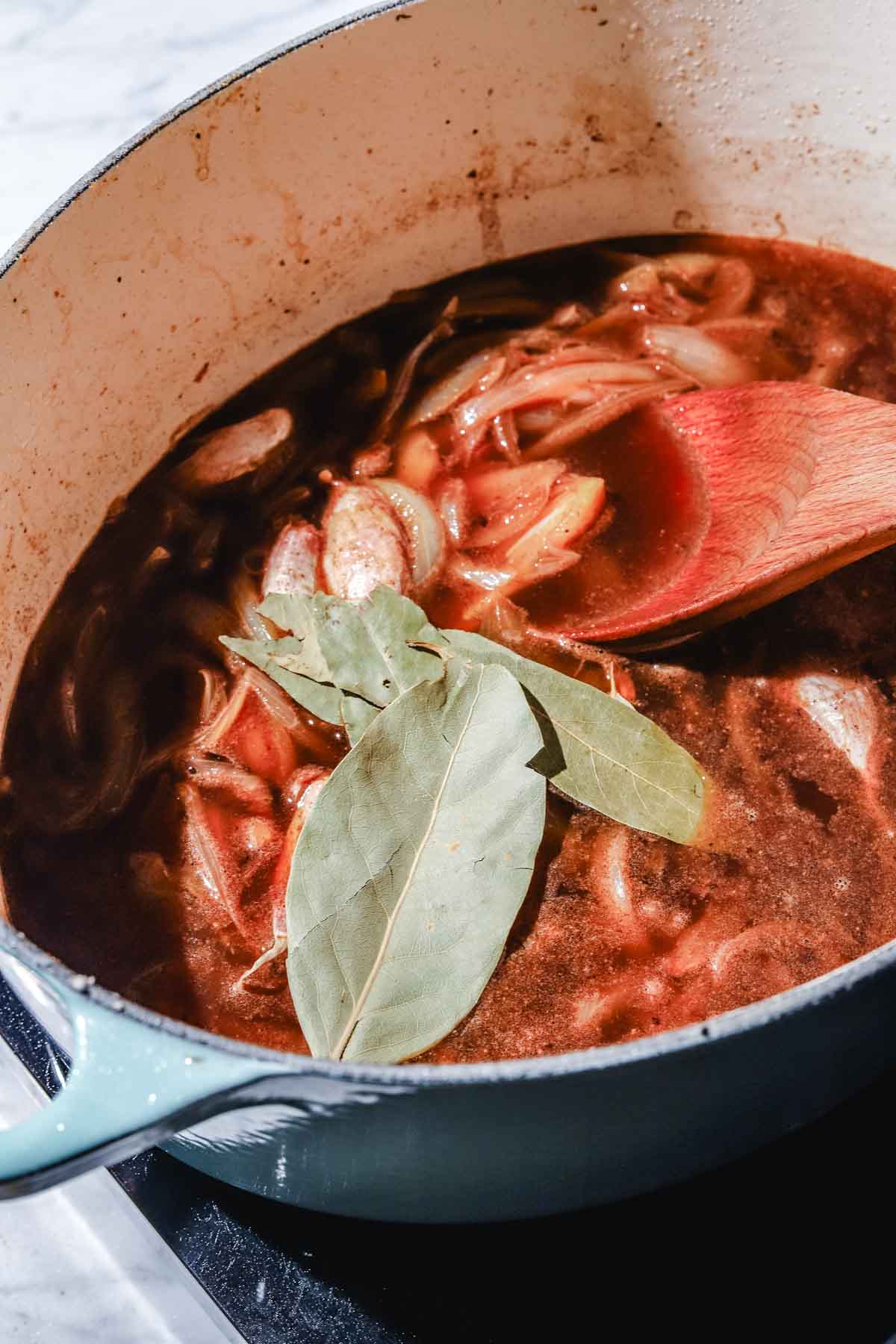 Sauteed onions with spices, broth and bay leaves in a large light mint pot on a marble background