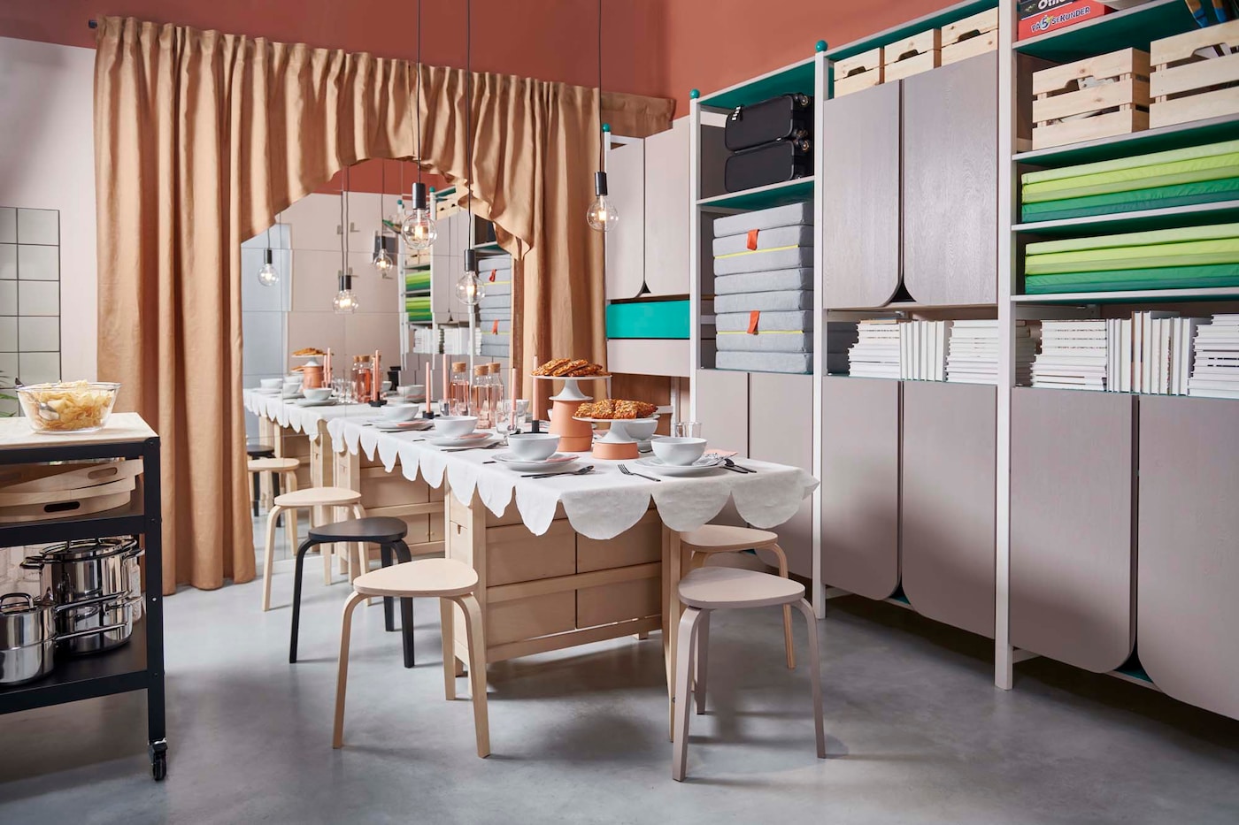 Wide view of a room with a long table set for a celebration, a large mirror wall framed by curtains, and a wall-to-wall storage unit.