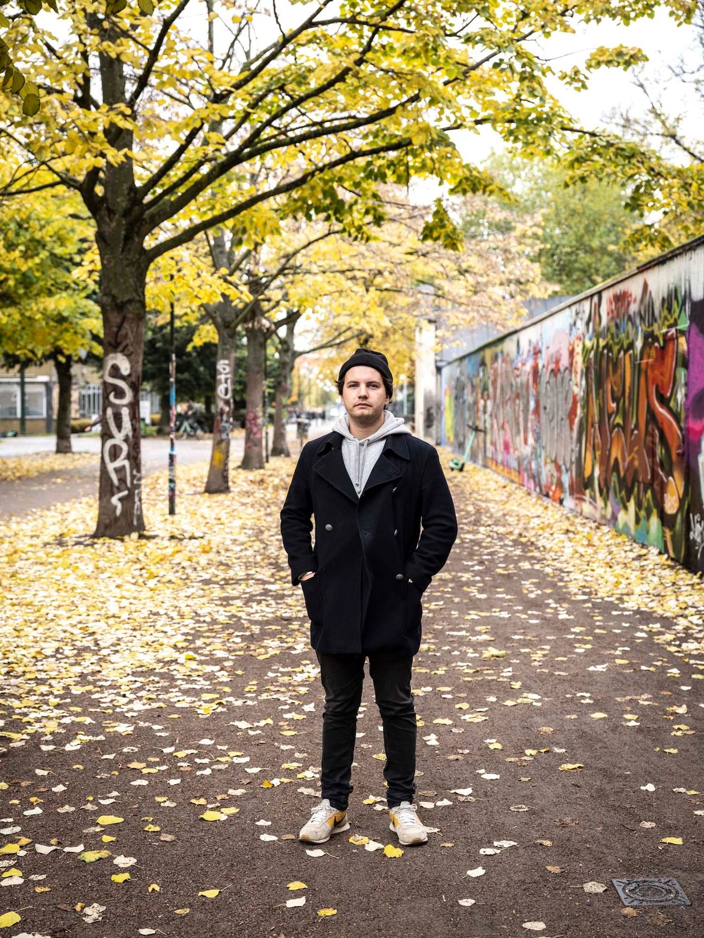 Linus stands on a sidewalk next to a wall covered in graffiti. 