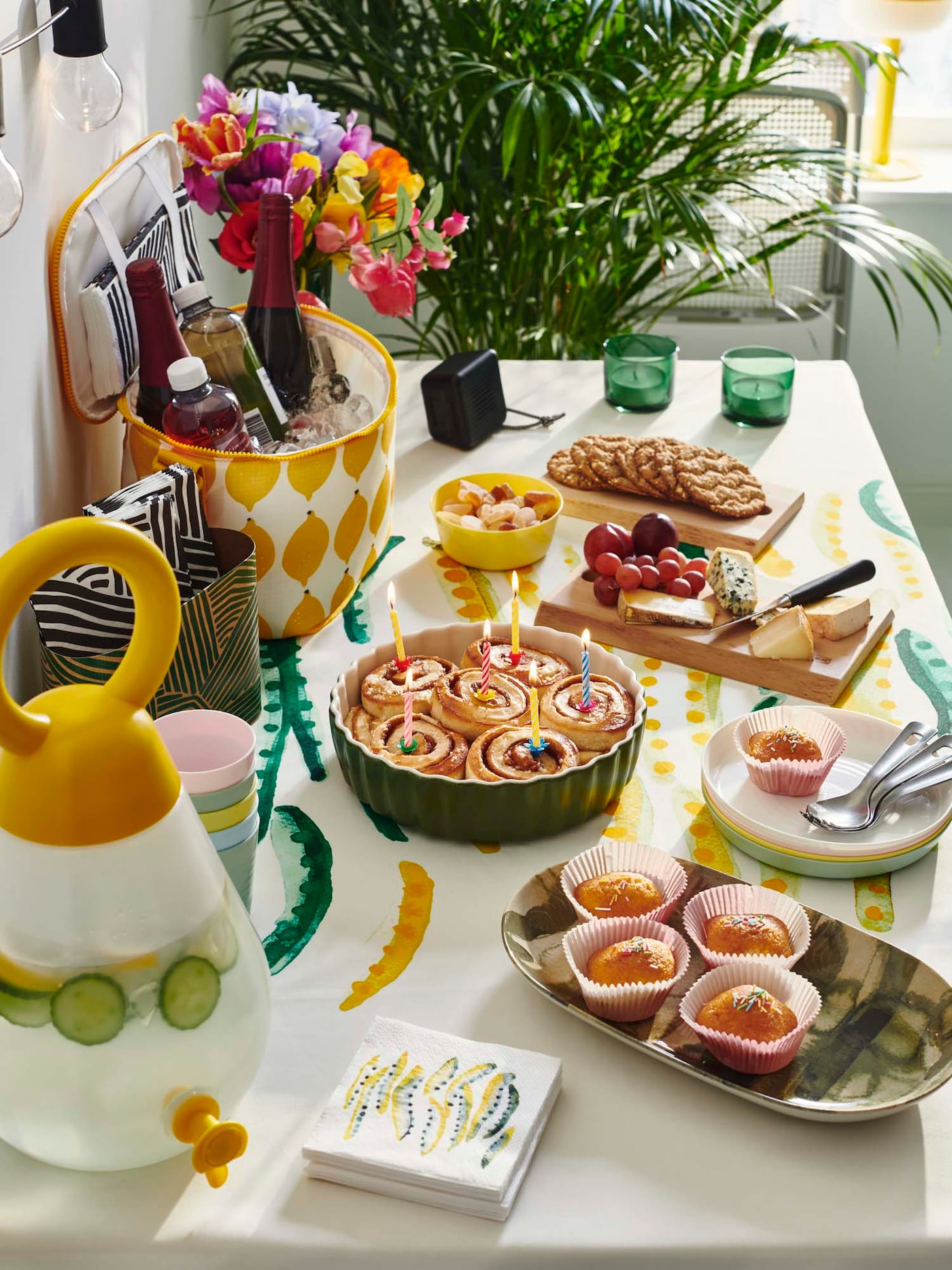 A casual celebration table spread with baked treats, cold drinks, fruit, cheese, candy and crackers. 