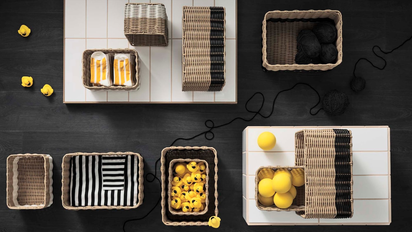 A dark surface with storage boxes in natural materials, filled with yellow or black and white objects.