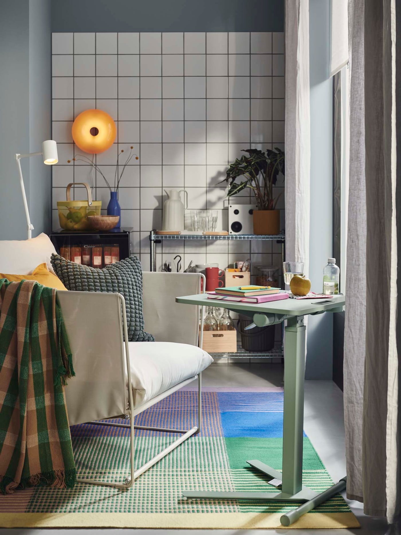 A room with a green MITTZON laptop table with castors in front of an armchair on top of a rug.