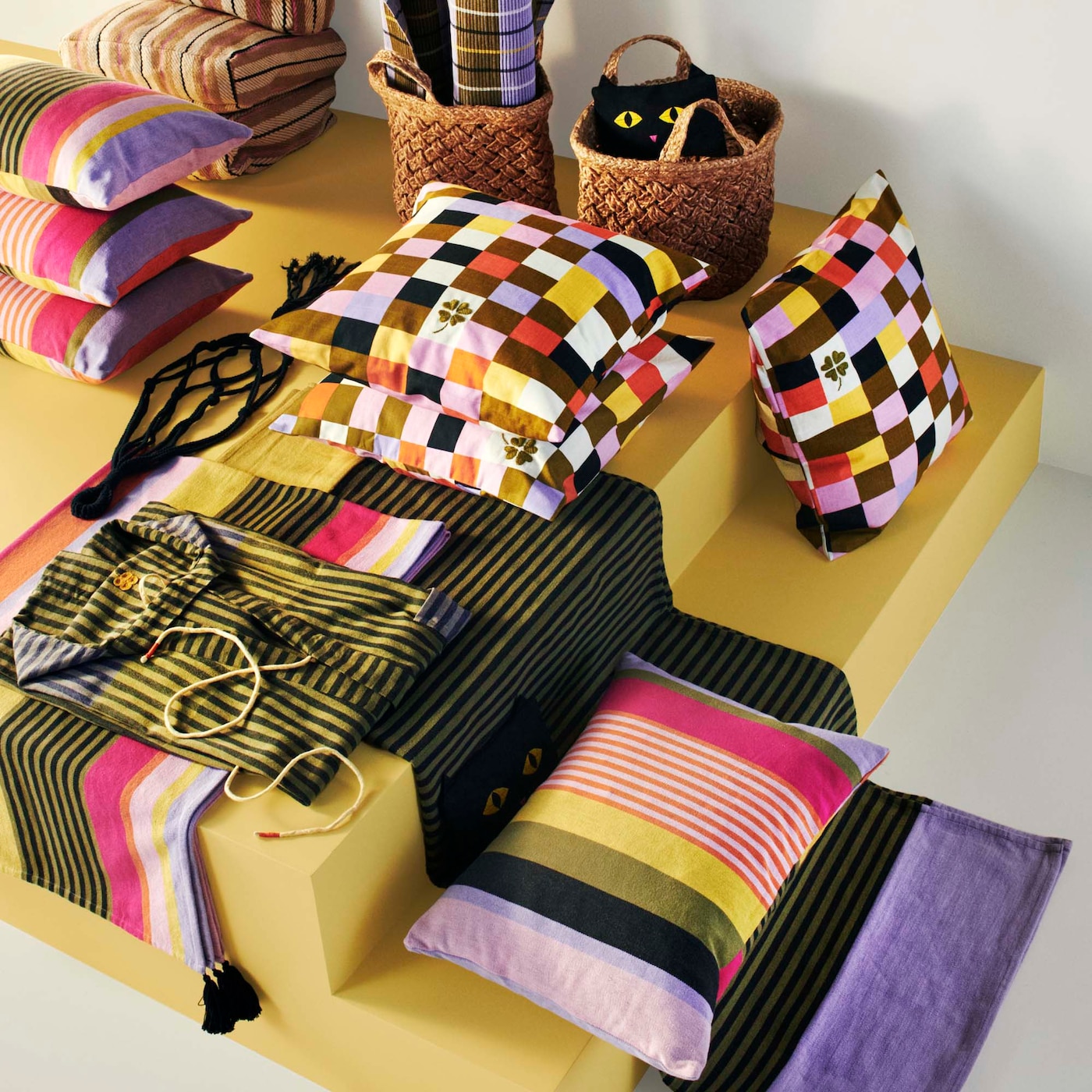 An aerial view of yellow podiums featuring brightly coloured and patterned throws, cushions and accessories from the MÄVINN collection.