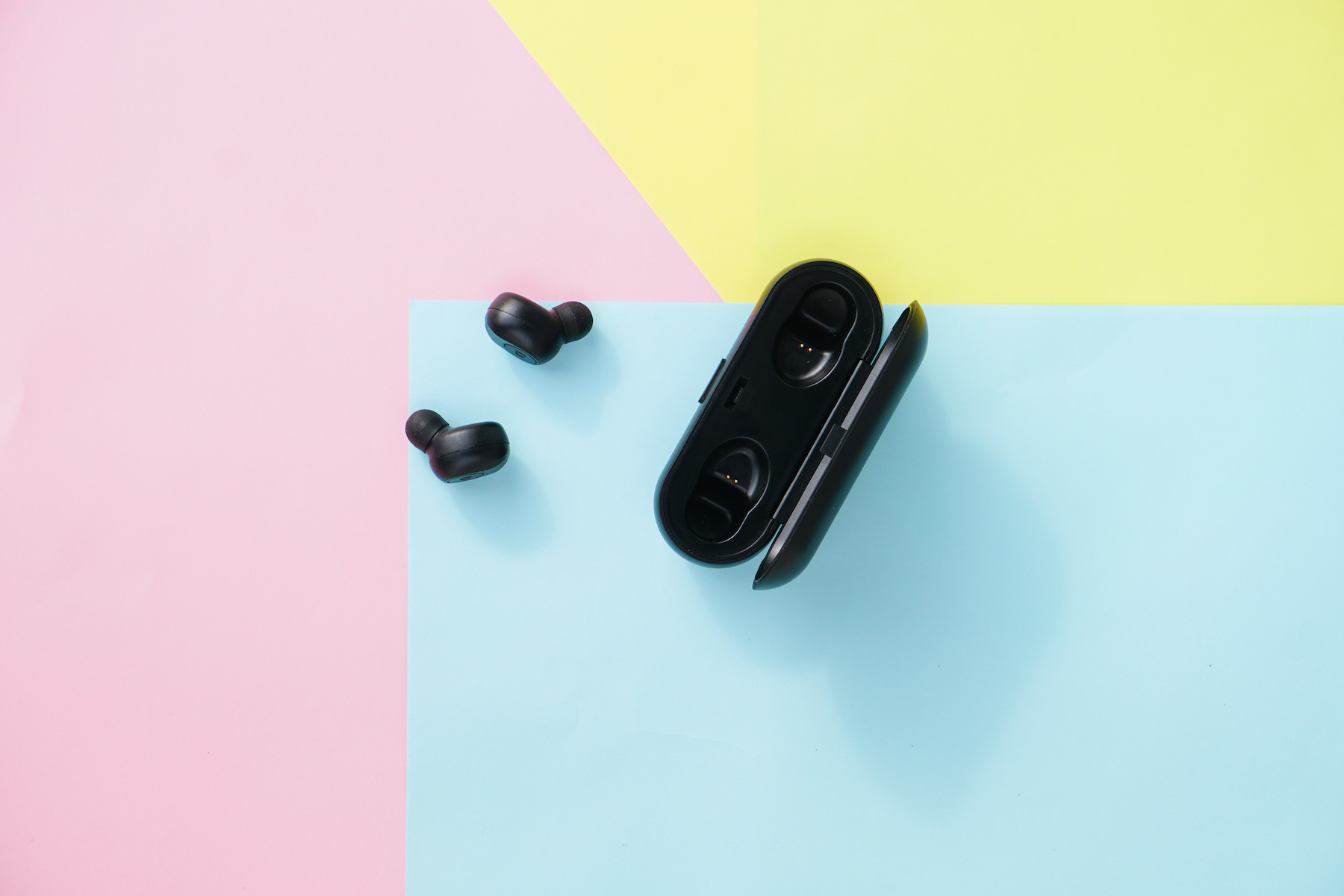 Black true wireless earbuds headphones with power bank case over colorful pastel color.