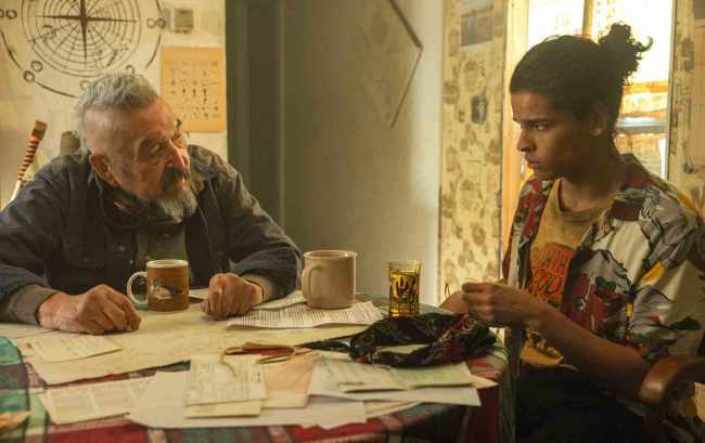 A teen boy and elderly man sitting at a dining table strewn with papers; still from 'Reservation Dogs'