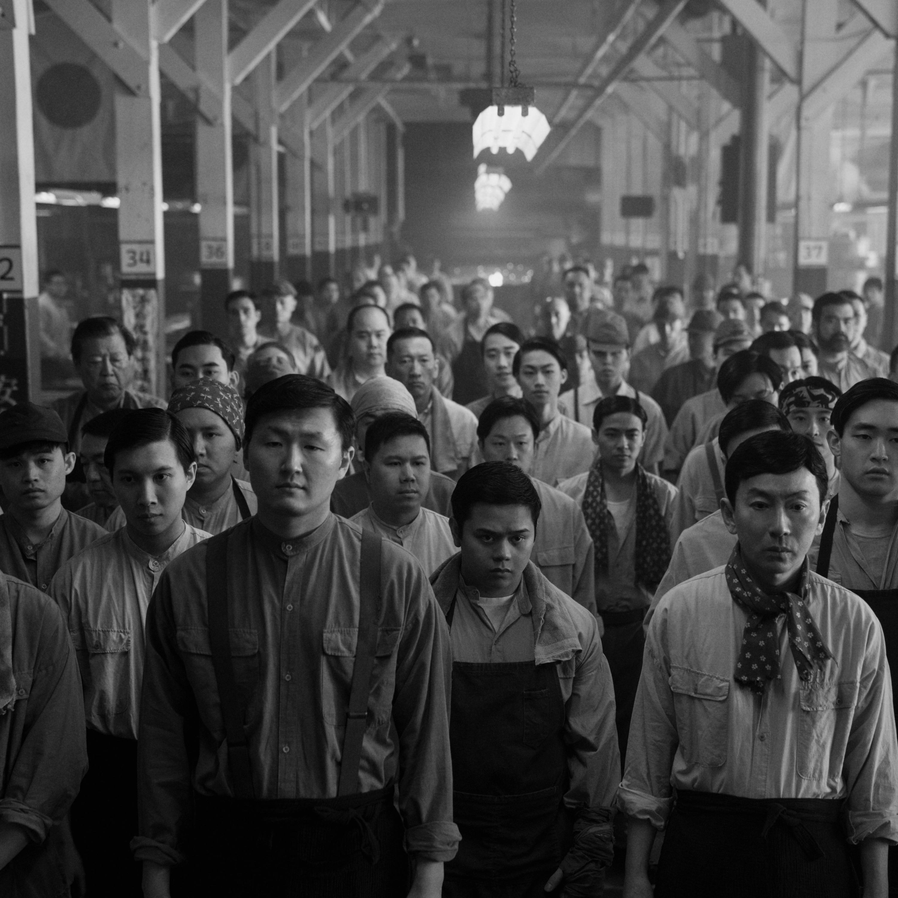 A black and white image of men lined up in a factory hall from Episode 5 of Season 2 of 'Pachinko'