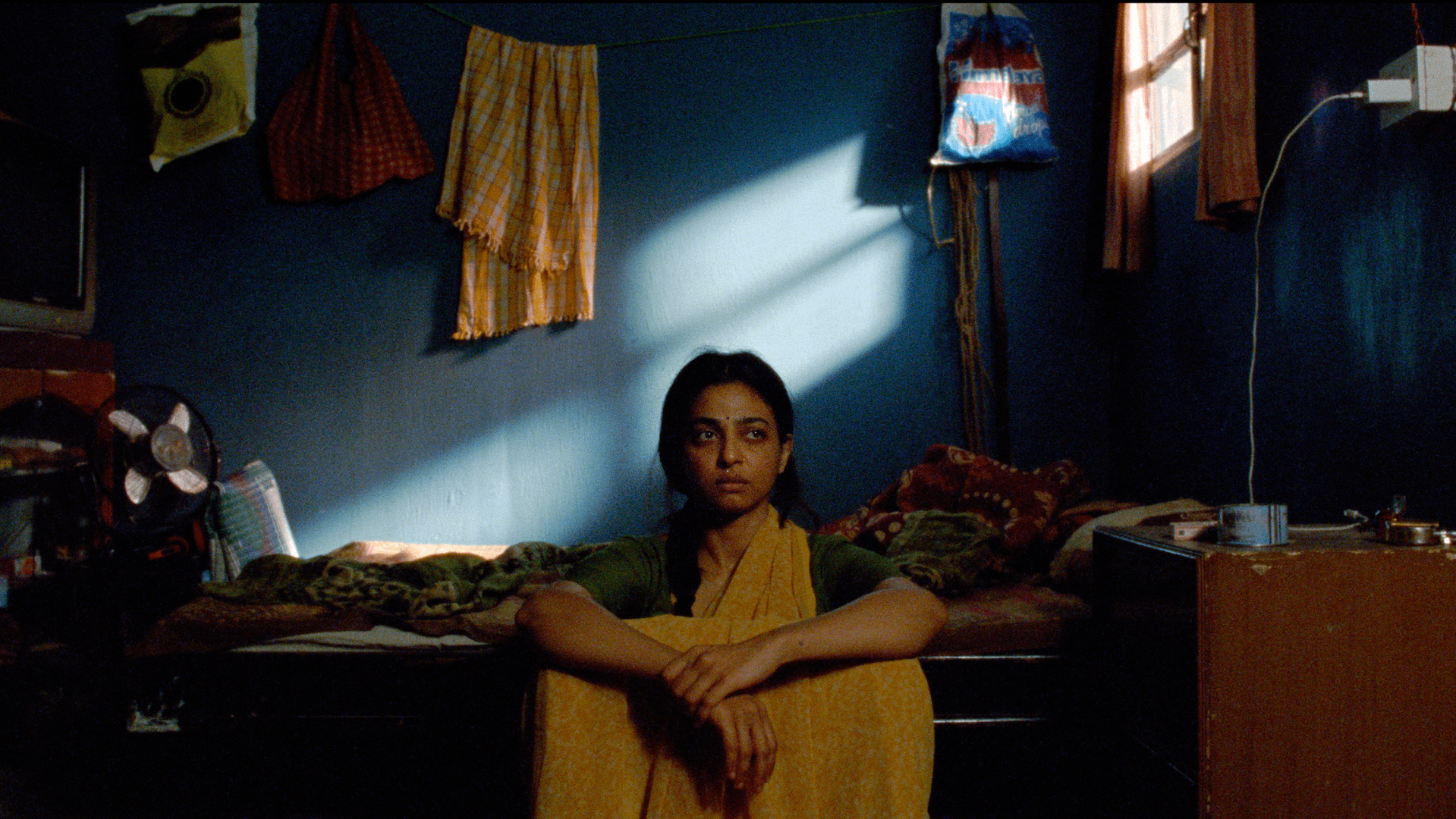 A woman in a yellow saree, sitting on the floor next to her bed with a look of despair; Radhika Apte in 'Sister Midnight'