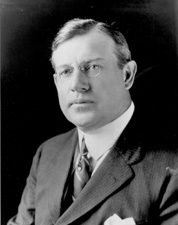 Bespectacled man with neatly combed dark hair, wearing a suit and tie.