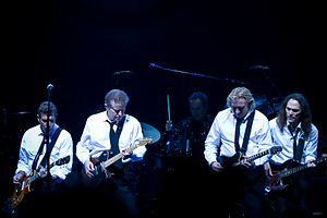 A color photograph of four members of the Eagles on stage with guitars